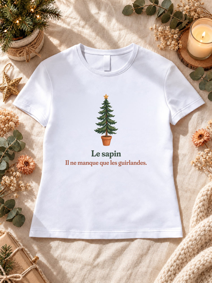 Visuel d’illustration – t-shirt blanc dans une mise en situation, avec le motif un sapin nu en pot et « Le sapin. Il ne manque que les guirlandes. »
