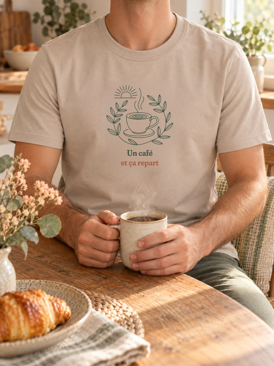 Visuel d’illustration – t-shirt dans une mise en situation, avec le motif une tasse de café fumante entourée d’une couronne de feuilles, sous un soleil levant et « Un café et ça repart »