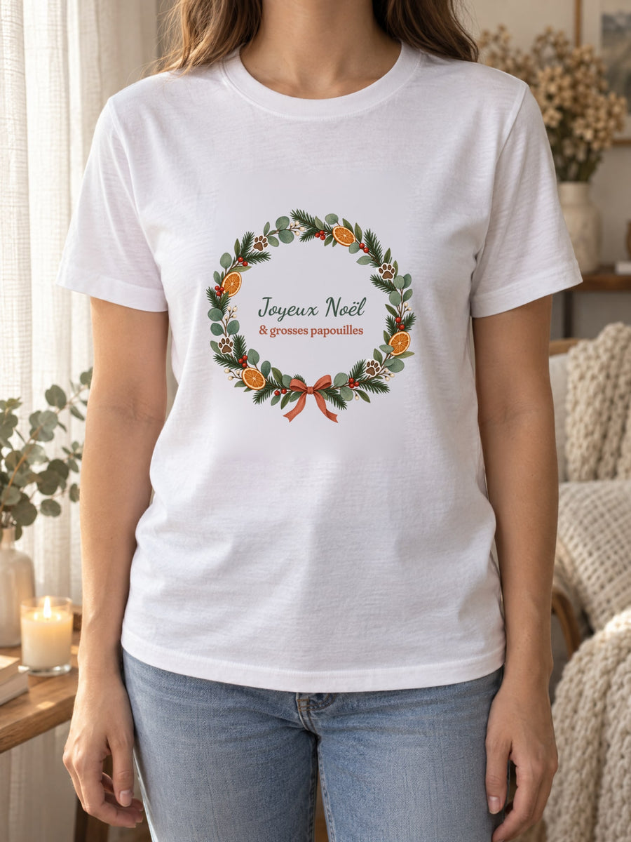 Visuel d’illustration – t-shirt blanc porté, près d’un rideau de lin et d’une bougie, avec le motif de Noël : une couronne de Noël avec des empreintes de pattes et le texte « Joyeux Noël & grosses papouilles »