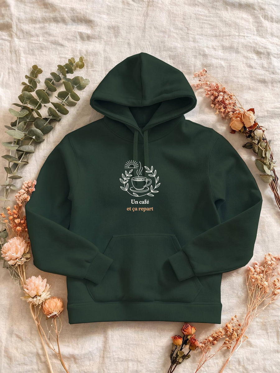 Visuel d’illustration – Sweat femme vert forêt avec le motif une tasse de café fumante entourée d’une couronne de feuilles, sous un soleil levant et « Un café et ça repart »