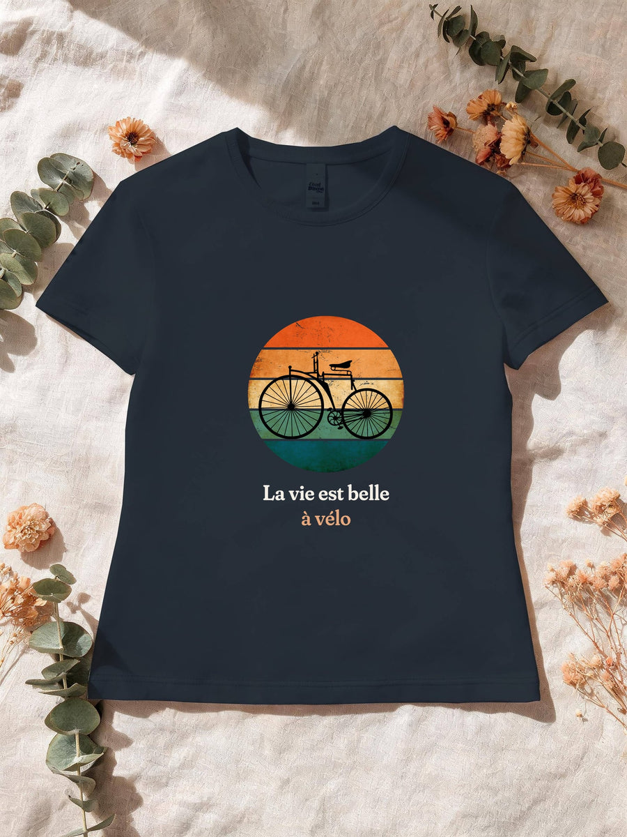 Visuel d’illustration – T-shirt femme navy avec le motif un vélo ancien à grande roue, en silhouette devant un soleil couchant à bandes rétro et « La vie est belle à vélo »