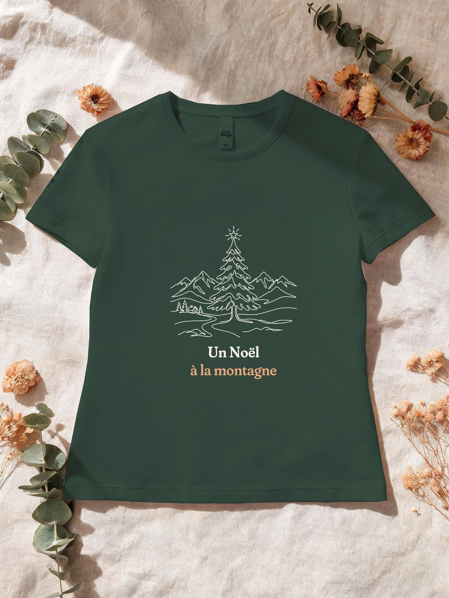 Visuel d’illustration – T-shirt femme vert forêt avec le motif un sapin de Noël étoilé devant des montagnes enneigées, dessiné au trait et « Un Noël à la montagne »