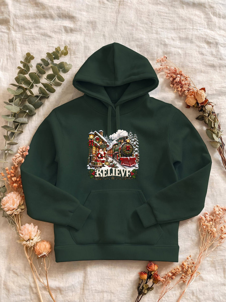 Visuel d’illustration – Sweat femme vert forêt avec le Père Noël et le train à vapeur devant la gare enneigée, « Believe »