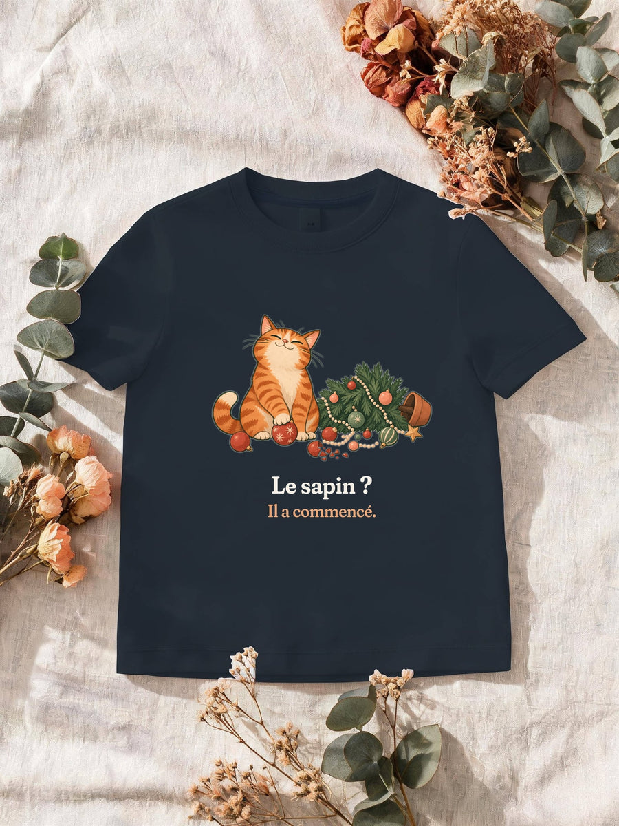 Visuel d’illustration – T-shirt homme navy avec le motif de Noël : un chat roux assis près d’un sapin de Noël renversé et la phrase « Le sapin ? Il a commencé. »