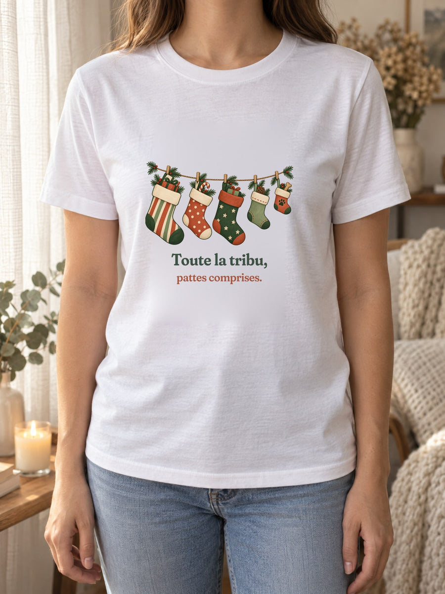 Visuel d’illustration – t-shirt blanc porté, près d’un rideau de lin et d’une bougie, avec le motif de Noël : une guirlande de chaussettes de Noël, dont une petite avec une empreinte de patte, et la phrase « Toute la tribu, pattes comprises. »