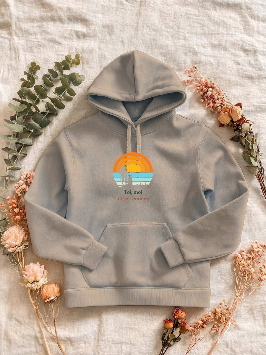 Visuel d’illustration – Sweat femme sable avec le motif un randonneur et son chien assis, en silhouettes devant un grand soleil orange à bandes rétro et « Toi, moi et les sentiers »