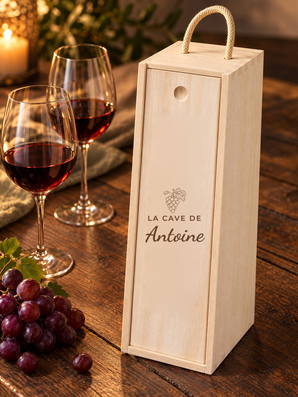 Visuel d’illustration – caisse à vin sur une table en bois foncé près de deux verres et de raisins, gravée « La cave de Antoine » (exemple)
