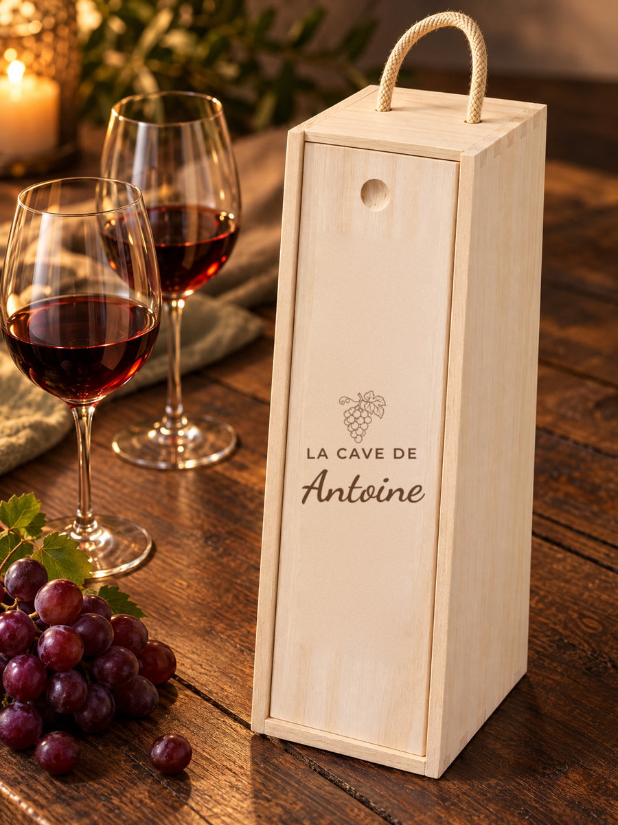 Visuel d’illustration – caisse à vin sur une table en bois foncé près de deux verres et de raisins, gravée « La cave de Antoine » (exemple)