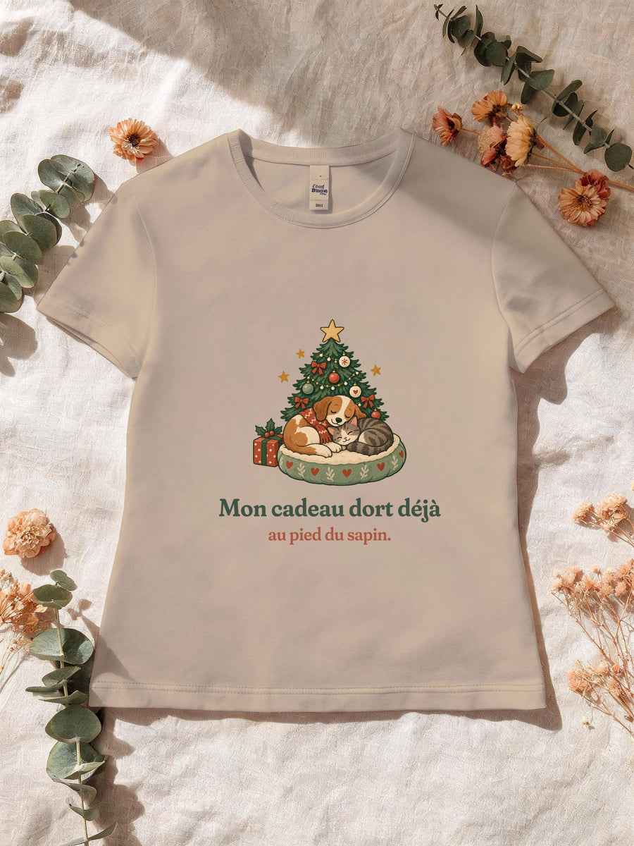 Visuel d’illustration – T-shirt femme sable avec le motif de Noël : un chien et un chat endormis au pied d’un petit sapin et la phrase « Mon cadeau dort déjà au pied du sapin. »