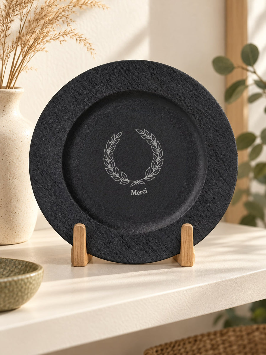 Visuel d’illustration – assiette noire debout sur un chevalet, gravée d’une couronne de laurier et « Merci » (exemple)