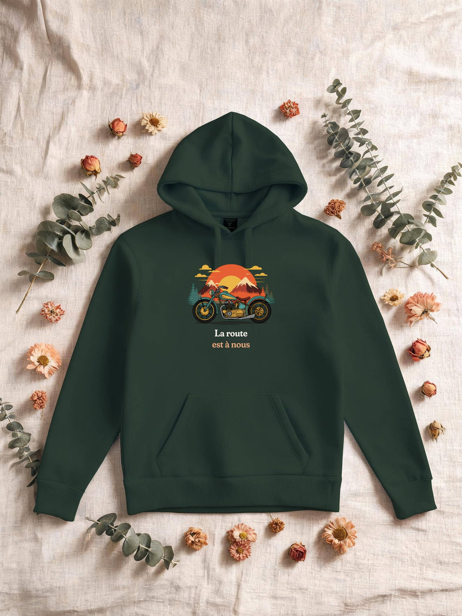 Visuel d’illustration – Sweat homme vert forêt avec le motif une moto ancienne illustrée en couleurs devant des montagnes, des sapins et un soleil couchant et « La route est à nous »