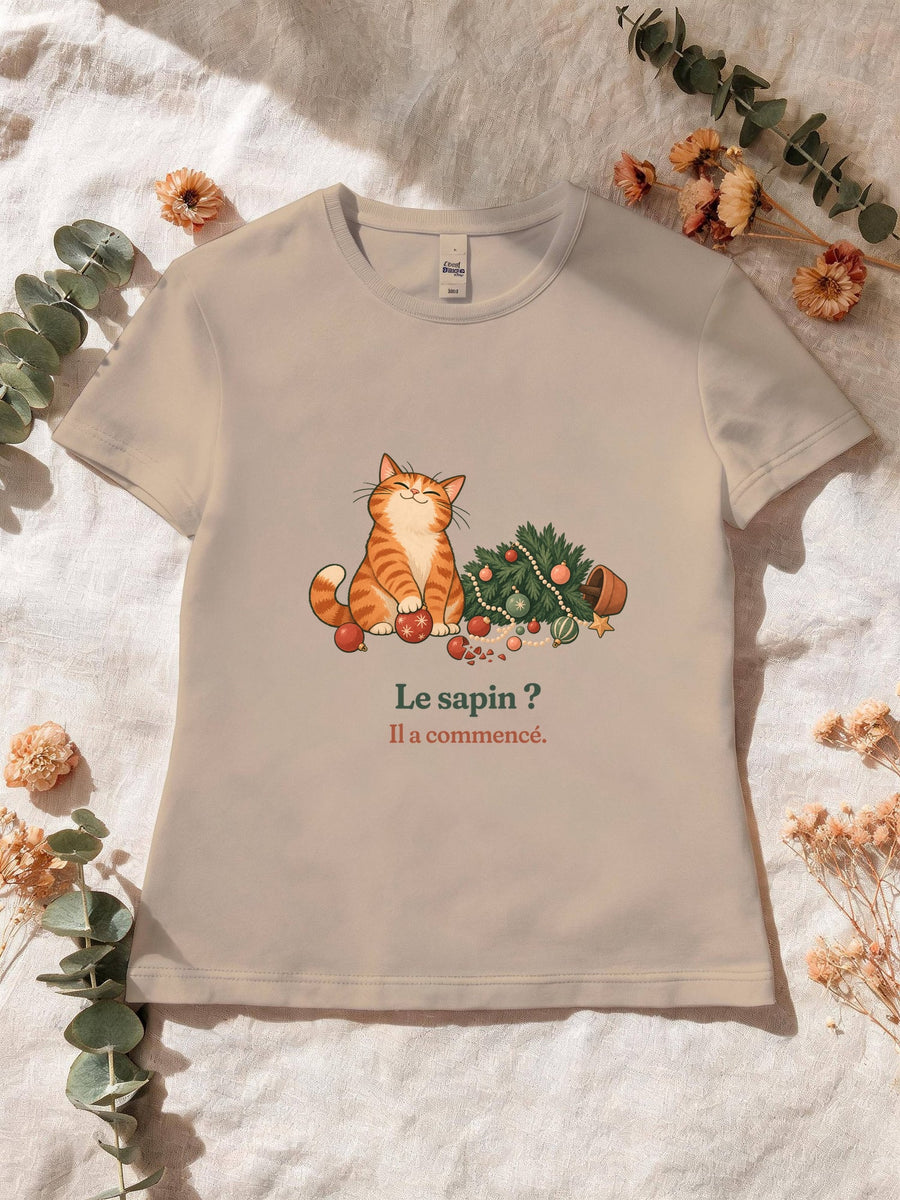 Visuel d’illustration – T-shirt femme sable avec le motif de Noël : un chat roux assis près d’un sapin de Noël renversé et la phrase « Le sapin ? Il a commencé. »