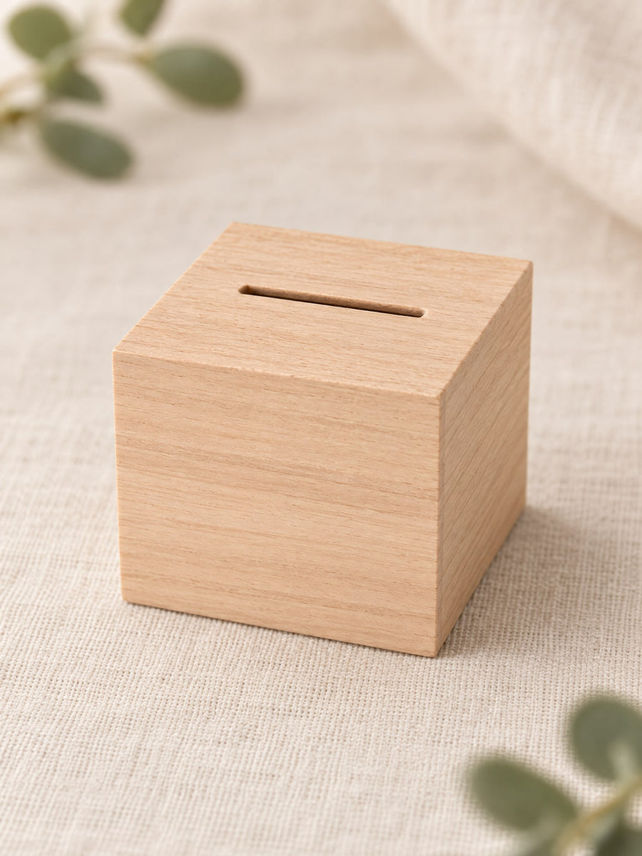 Visuel d’illustration – tirelire cube en bois clair vierge, posée sur un lin crème