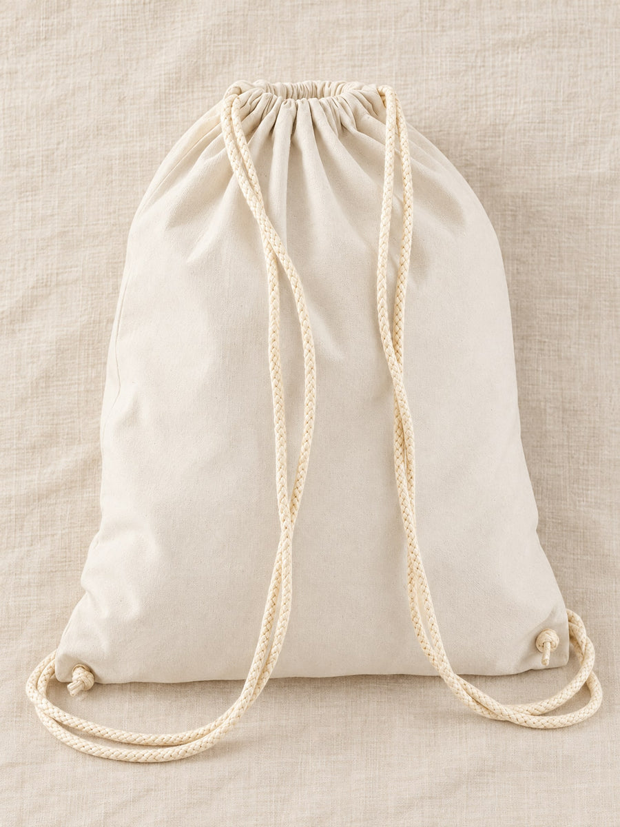 Visuel d’illustration – sac à dos à cordon en coton naturel vierge, posé à plat sur un lin crème