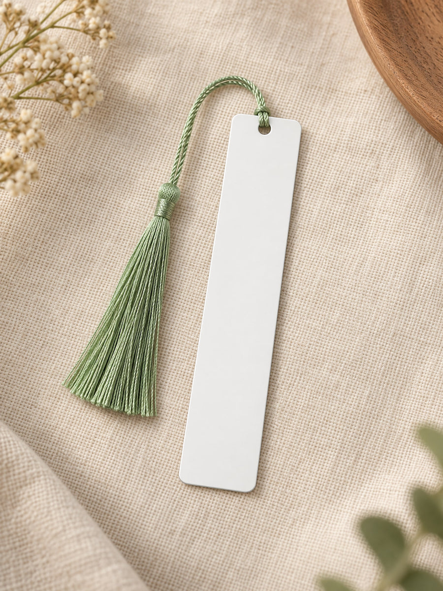 Visuel d’illustration – marque-page en métal blanc vierge avec son pompon vert sauge, posé sur un lin crème