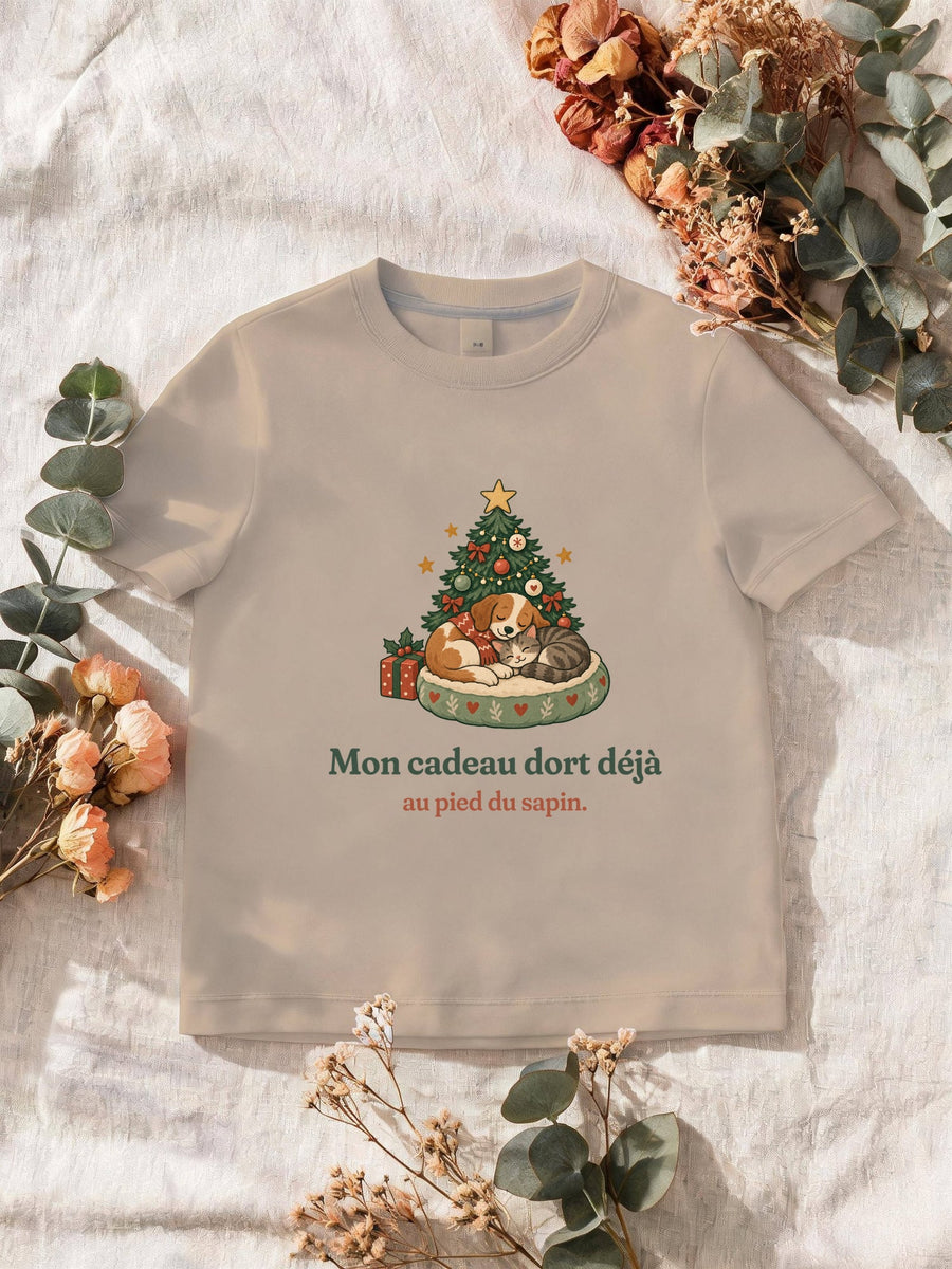 Visuel d’illustration – T-shirt homme sable avec le motif de Noël : un chien et un chat endormis au pied d’un petit sapin et la phrase « Mon cadeau dort déjà au pied du sapin. »