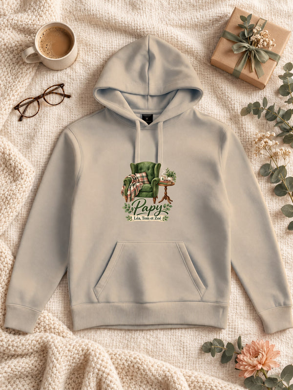 Visuel d’illustration – Sweat à capuche sable personnalisé « Le fauteuil de Papy » avec les prénoms Léa, Tom et Zoé, posé à plat